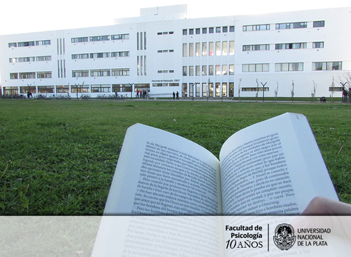 Vista de la fachada de la Facultad de Psicología de la UNLP. Libro impreso en primer plano.